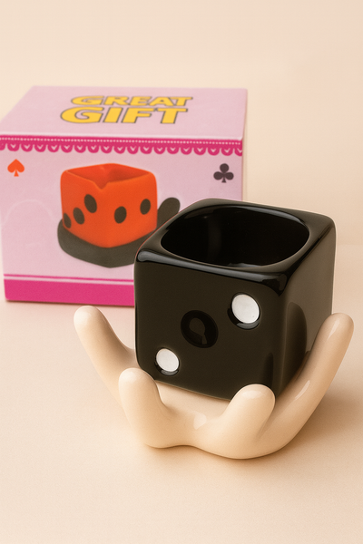 Black dice-shaped mug with white dots on a beige background, next to a pink box labeled 'Great Gift'.